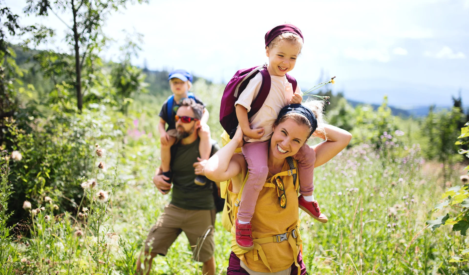 Eine Familie in der Natur, die Mutter trägt ein Kind auf den Schultern | © Halfpoint / Adobe Stock